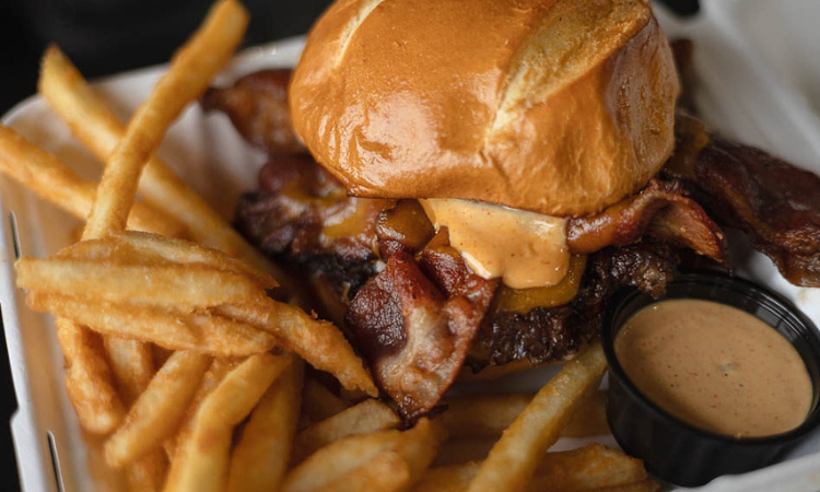 The Smash Squatch: loaded smash burger with four thick slices of bacon, double cheddar, and SMASH sauce on a pretzel bun, served with fries.