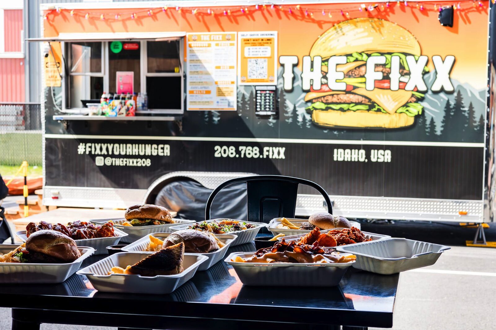 A full spread of smash burgers, smothered fries, and wings on the table at The Fixx Smash Burgers food truck in Post Falls, Idaho.